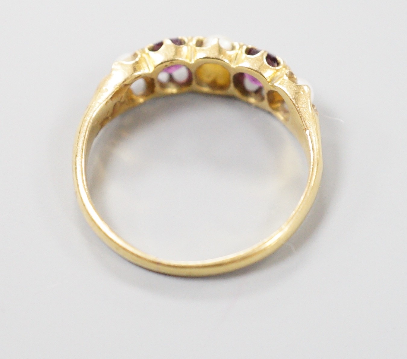 A yellow metal two stone garnet, three stone split pearl set half hoop ring, size K, gross 2.4 grams.
